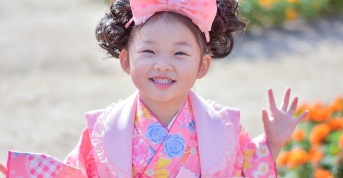 ピンクの被布を着て手を振る3歳の女の子