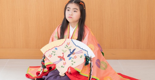 扇子を手に持ち座っている十二単姿の7歳女児