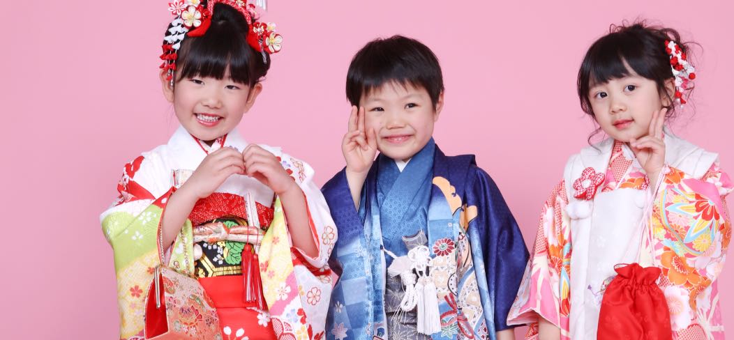 ピンクの背景の前に並ぶ着物姿の3人の子ども