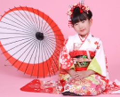 開いた番傘を背に座る着物姿の女児