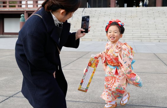大殿の前で千歳飴を持つ女の子をスマートフォンで撮る母親